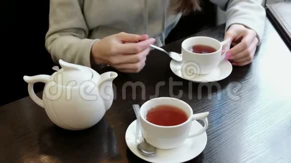 特写的女人她的手在茶里用勺子糖搅拌桌子上有茶壶和杯子视频的预览图