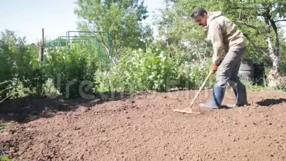 一个人是郊区一个穿着橡胶靴的农民一个菜园在锄头的帮助下割草视频的预览图