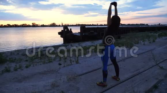 美丽苗条的年轻女子从事健身表演力量练习黎明时分沿着沙漠码头视频的预览图