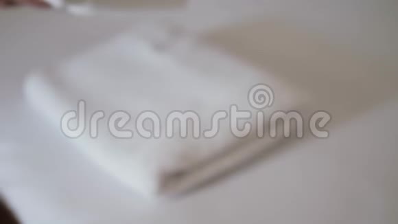 双手特写把一叠新鲜的白色浴巾放在床单上客房服务员清洁酒店客房视频的预览图
