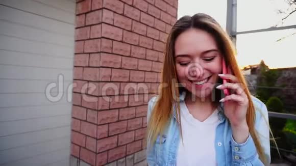 漂亮的女孩用智能手机在外面用粉红色的盒子说话微笑着视频的预览图