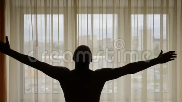 成年白种人运动员站在窗前日出时举起双手男人的剪影他很自由视频的预览图