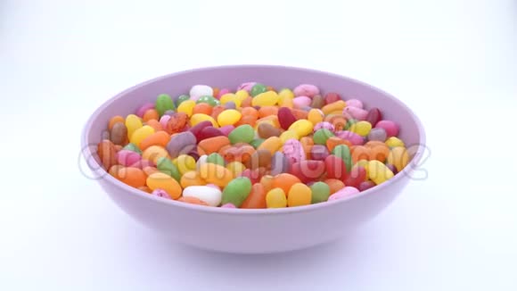 一堆小豆形糖冻糖果在转盘上的紫色碗里旋转孤立无援视频的预览图