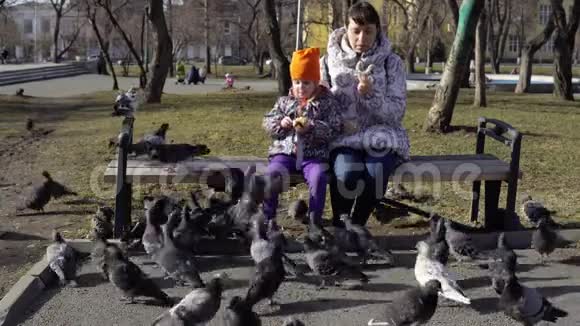 一个年轻的女人和一个小女孩在寒冷的阴天吃面包和喂鸽子视频的预览图