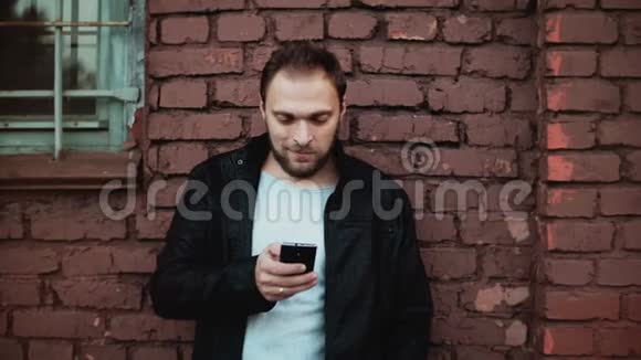在外面使用智能手机的随便白人英俊的胡须年轻的男性商人发短信红砖墙4K视频的预览图