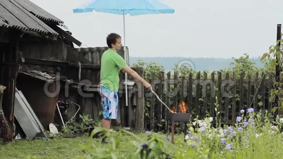 带着雨伞的人在火旁烧烤雨在下一座背景有栅栏的老建筑视频的预览图