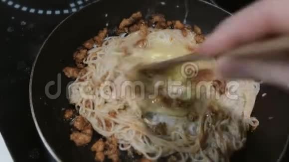 一个男人的手用木铲意大利面条碎肉和鸡蛋在平底锅中混合视频的预览图