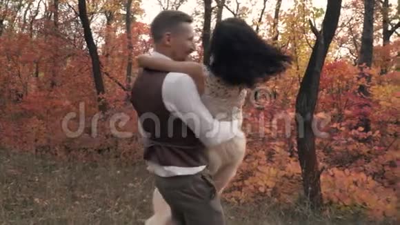 一个穿着西装的快乐男人穿着一个穿着白色裙子的女人在秋天公园的中央慢动作视频的预览图