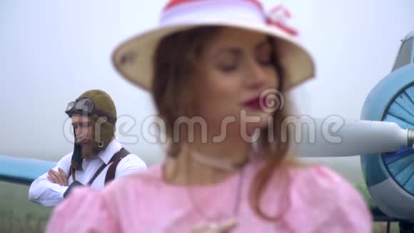 与一个老飞行员重新聚焦在一个穿着粉红色连衣裙和一顶60年代慢动作风格帽子的女人身上视频的预览图