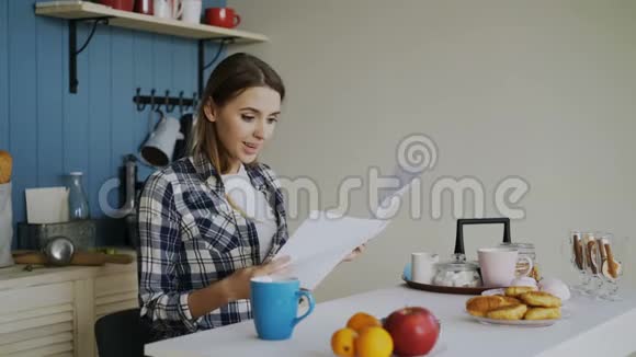 年轻快乐的女人在家吃早餐的时候惊讶地在厨房里听到好消息视频的预览图