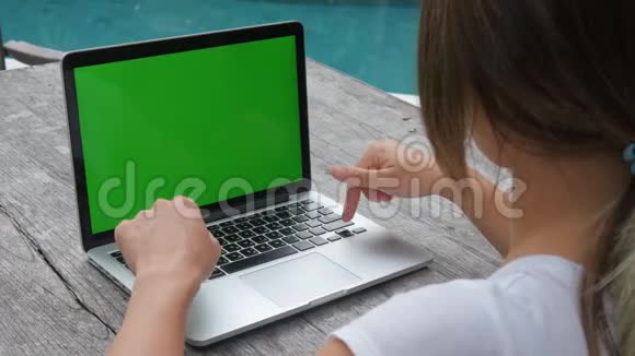 女人在笔记本电脑绿屏工作室外整洁的游泳池工作和旅行视频的预览图