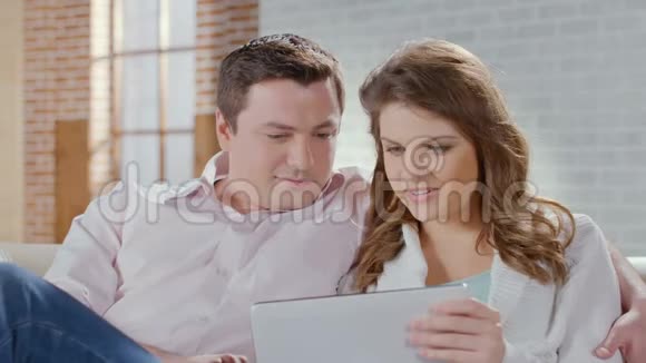 情侣聊天在平板电脑上看照片在客厅里笑视频的预览图