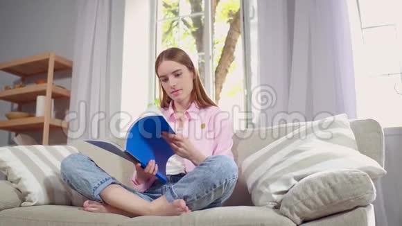 年轻女子坐在沙发上看杂志视频的预览图