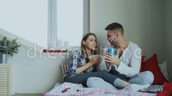 快乐的年轻夫妇在床上谈笑风生早上在家喝咖啡视频的预览图