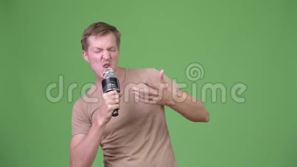 年轻英俊的斯堪的纳维亚男子在绿色背景下唱歌视频的预览图