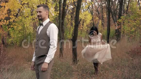 一个穿着裙子的快乐女人跑到男人的身后跳到他的背上在秋天的公园里慢镜头拍摄视频的预览图