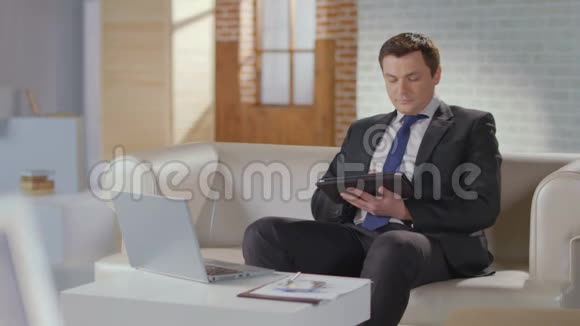 英俊的男士西装在平板电脑上工作对着相机微笑视频的预览图
