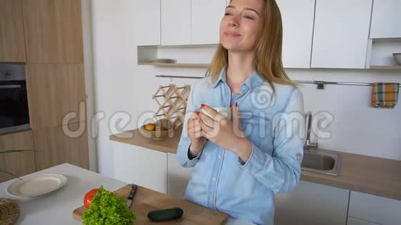 年轻的女人高兴地开始新的一天手里拿着一杯茶早上站在厨房的餐桌上视频的预览图