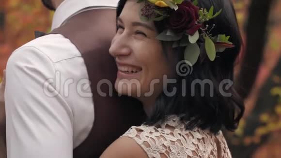 一个女人穿着白色连衣裙头上戴着花环拥抱着一个男人在一个秋天的公园里笑着慢慢地视频的预览图