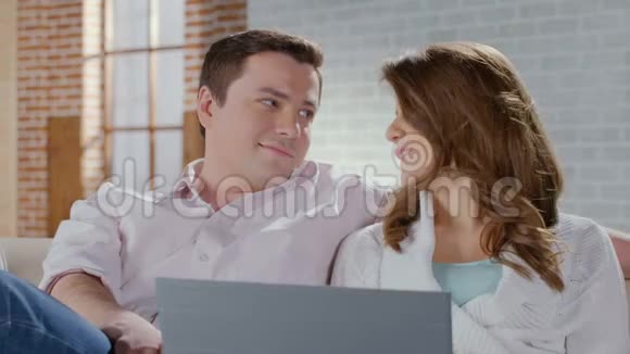 美丽的妻子和丈夫蜷缩在沙发上在网上购物视频的预览图