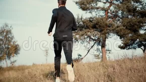 慢动作的人跑上草山低角度后视年轻的男性在秋天的乡村风景中徘徊视频的预览图