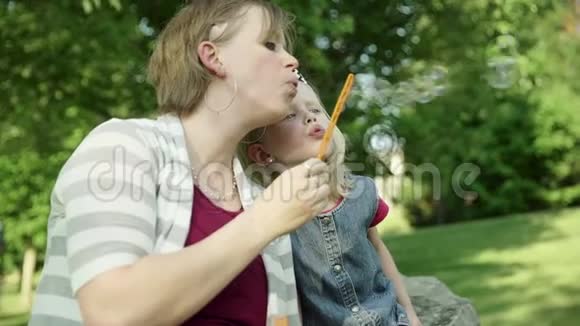 快乐的年轻妈妈和女儿在夏天的公园里吹肥皂泡视频的预览图