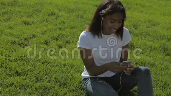 年轻女士坐在公园里享受音乐视频的预览图