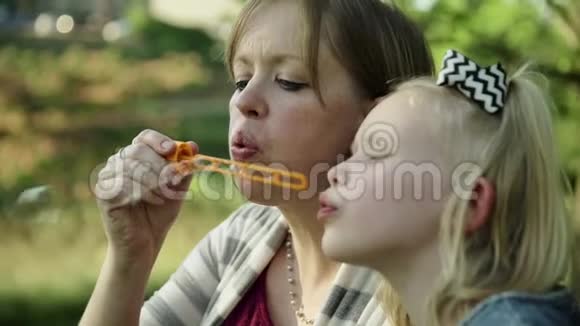 快乐的年轻妈妈和女儿在夏天的公园里吹肥皂泡视频的预览图
