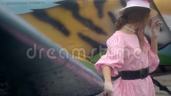 一个穿着粉红色长裙的沉思的女人正和一只画着画的老虎站在飞机旁动作缓慢视频的预览图