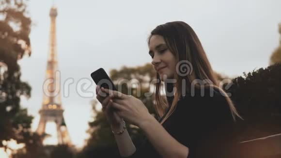 漂亮的年轻女人用智能手机快乐的女性坐在法国巴黎埃菲尔铁塔附近的长凳上视频的预览图