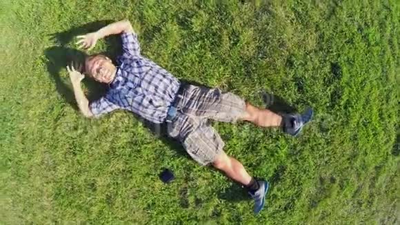 年轻的微笑男性躺在草地上空中垂直拍摄放大视频的预览图