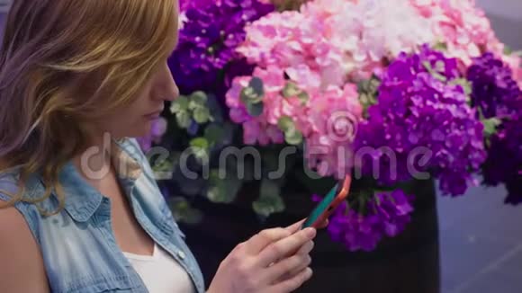 一位美丽的年轻女子坐在一个靠近花坛的大型现代购物中心的长凳上她利用她视频的预览图