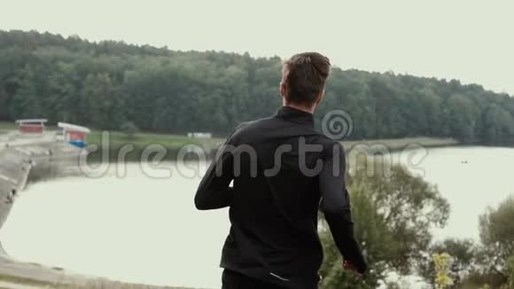 慢动作从山上跑到湖边的人镜头跟随着年轻的男子下山背景视图视频的预览图