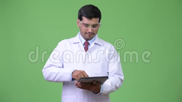年轻英俊的波斯医生戴着防护眼镜使用数码平板电脑视频的预览图