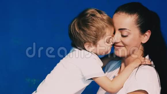 母亲和儿子在蓝色背景上玩笑和亲吻视频的预览图