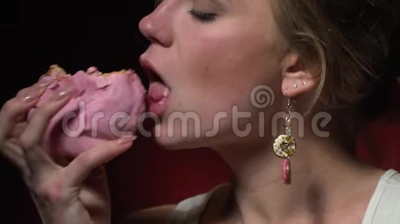 慢镜头拍摄一个金发女郎咬一个带粉色釉的甜甜圈视频的预览图