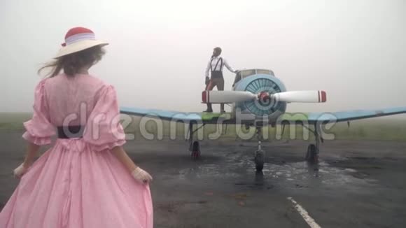 一位60岁的女士穿着粉色连衣裙来到一架老式飞机上飞机上站着飞行员视频的预览图
