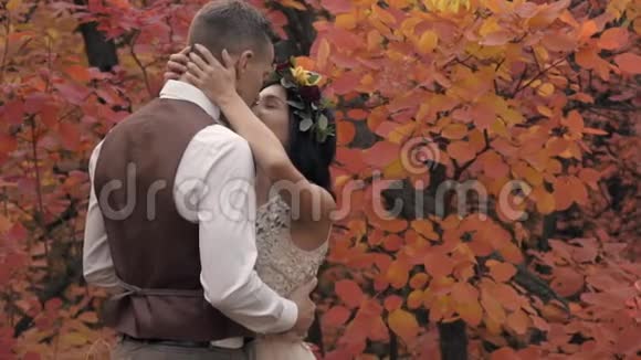 一个穿着西装的男人轻轻地吻着一个穿着白色裙子的女孩站在一个秋天公园的中央花圈视频的预览图