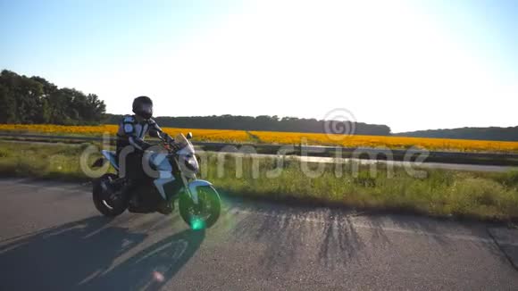 摩托车手驾驶摩托车在乡间小路上背景是向日葵田戴头盔的年轻人视频的预览图