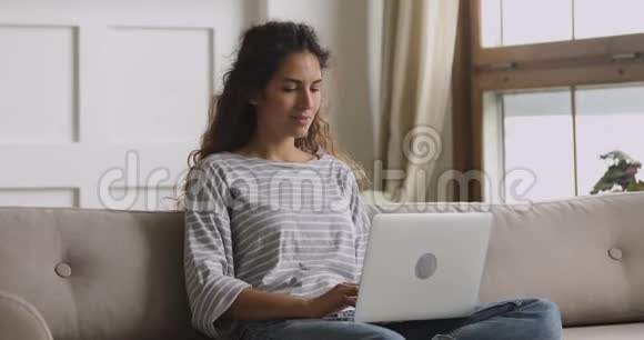 坐在沙发上用笔记本电脑打字微笑的年轻女子视频的预览图