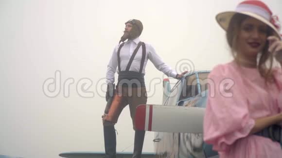 重新聚焦于一个在雾中站在飞机机翼上的野蛮飞行员她身上穿着粉红色连衣裙和白色帽子的女人视频的预览图