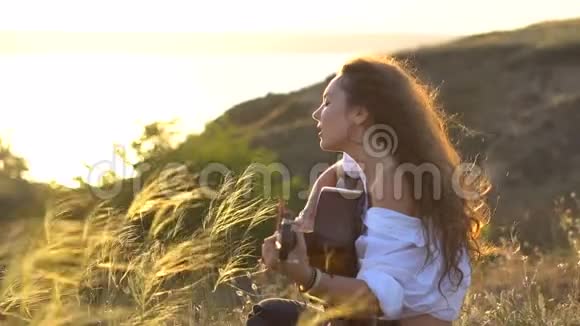 CurlyGipsy深色头发的女孩在海湾斜坡上弹吉他唱歌视频的预览图