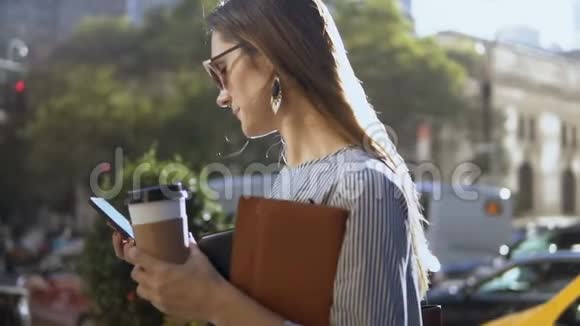 阳光明媚的一天年轻的快乐女商人在市中心用智能手机拿着咖啡和文件慢动作视频的预览图