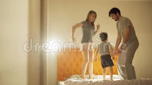 幸福的家庭和小儿子在晚上睡觉前在家里的床上跳舞视频的预览图