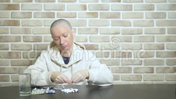 一个年轻的秃头女人坐在一张靠在砖墙上的桌子旁悲伤地看着药丸复制空间视频的预览图