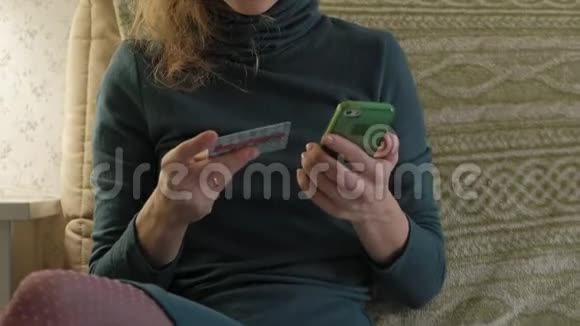 一个穿着绿色衣服的年轻女子坐在沙发上手提电脑用电话和塑料卡工作学习视频的预览图