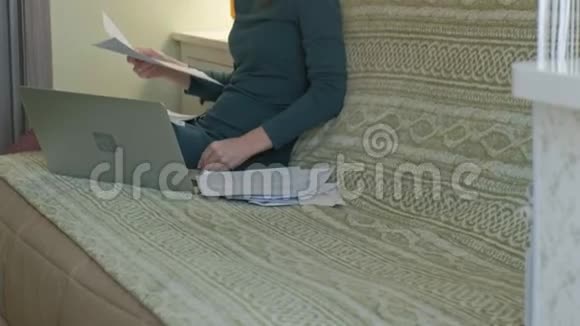 年轻女子穿着绿色连衣裙坐在沙发上手提电脑工作学习文件喝茶在家工作视频的预览图