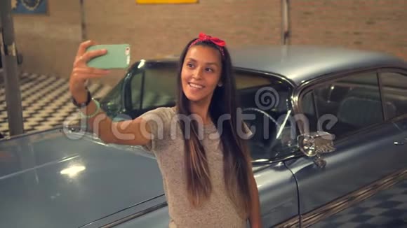 年轻的HipserPinup混合种族女孩带着手机在老式车库和旧车4K慢动作视频的预览图