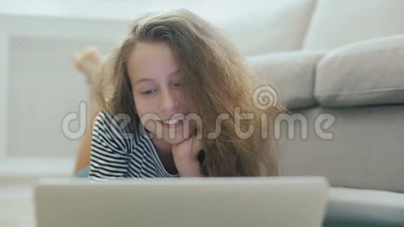 地毯上可爱的少女用笔记本电脑工作stadicam拍摄的快乐少女靠近一个有笔记本电脑的沙发少女使用视频的预览图