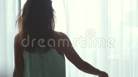 年轻美丽的黑发女人在她舒适的家拉开窗帘看着城市的景色在家放松的早晨视频的预览图